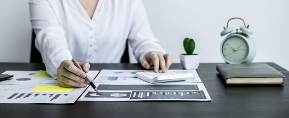 Close-up of a business woman holding a pen and pointing at a financial data sheet and pressing a calculator, she is checking monthly financial documents from the finance department. Financial concept.