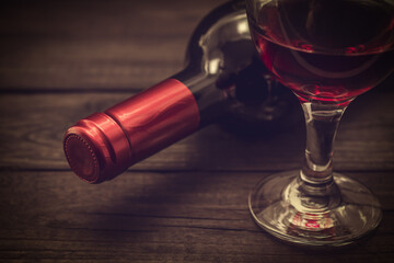 Bottle of red wine with a glass of red wine on an old wooden table. Close up view, focus on the bottle of red wine