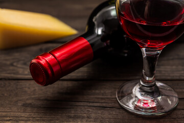 Bottle of red wine with a glass of red wine and a piece of parmesan on an old wooden table. Close up view, focus on the bottle of red wine