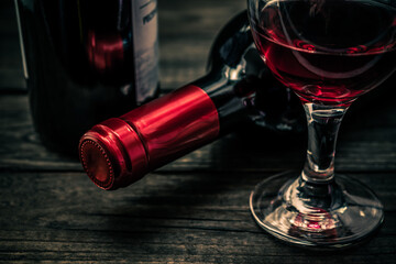 Two bottles of red wine with a glass of red wine on an old wooden table. Close up view, focus on the bottle of red wine