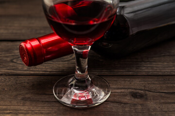 Bottle of red wine with a glass of red wine on an old wooden table. Close up view, focus on the glass of red wine