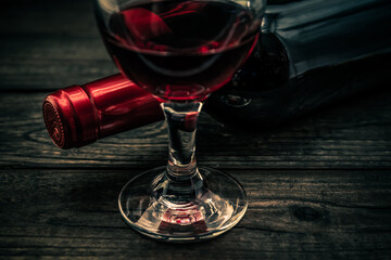 Bottle of red wine with a glass of red wine on an old wooden table. Close up view, focus on the glass of red wine