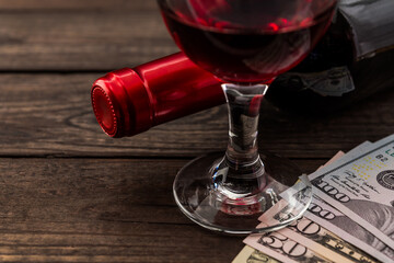Bottle of red wine with a glass of red wine and money on an old wooden table. Close up view, focus on the glass of red wine
