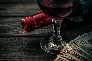 Bottle of red wine with a glass of red wine and money on an old wooden table. Close up view, focus on the glass of red wine