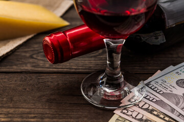 Bottle of red wine with a glass of red wine and a piece of parmesan with money on an old wooden table. Close up view, focus on the glass of red wine