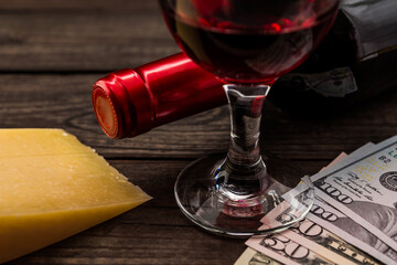 Bottle of red wine with a glass of red wine and a piece of parmesan with money on an old wooden table. Close up view, focus on the glass of red wine