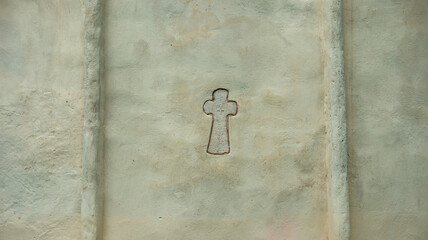 christian cross on white wall of stone church