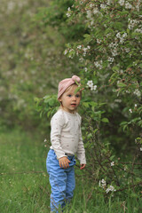 the baby stands and looks to the side near the blooming cherry bushes