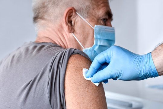 Elderly Man In Face Mask Getting Covid Vaccine. Doctor Giving Injection To Senior Man At Hospital. Virus, COVID-2019, Flu Protection. Vaccination Of Old Patient In Clinic During Coronavirus Pandemic.