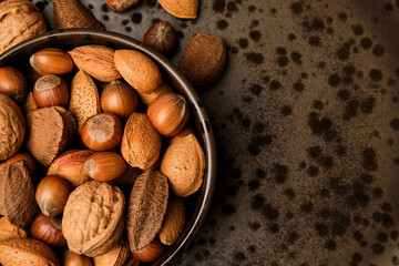 Almonds, walnuts and hazelnuts sitting in a brown bowl on a dark brown spotted plate.
