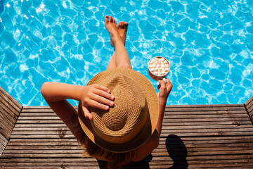 A cute little girl in a hat sits by the pool and holds a cup of cocoa and marshmallows. Beautiful...