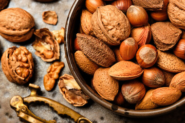 Almonds, walnuts and hazelnuts are sitting in a brown bowl and a nutcracker on a dark brown spotted plate.