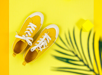 Yellow sneakers on yellow background with tropical leaf shadow. Trendy background. Mockup, summer holidays, vacation, travel, fashion concept