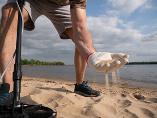 Guy on a sandy coast looking for treasure with a metal detector on a sunny summer day.