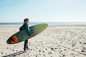 Girl surfer with surfboard, girl carrying his surfing board approaching to the beach