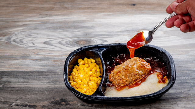 Adding sauce to a rib tv dinner in a black plastic tray