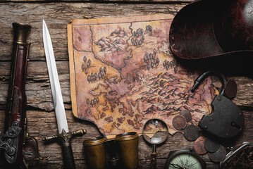 Old treasure map, coins, compass, weapon and pirate hat on the old wooden table flat lay background.