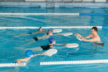 A group of boys and girls train and learn to swim in the pool with an instructor. Development of children's sports.