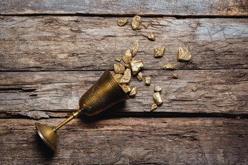 Golden goblet full of gold ore on the old wooden table flat lay background. Wealth concept.