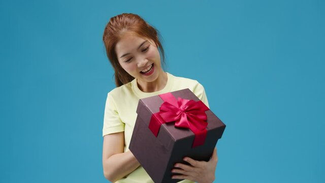 Young Asia girl smile and holding opened present box isolated over blue background. Copy space for place a text, message for advertisement. Advertising area, mockup promotional content.