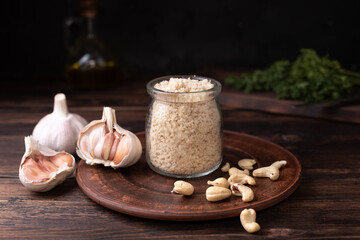Cashew nut parmesan, vegetarian cheese in glass jar with garlic on a wooden background, vegan food.
