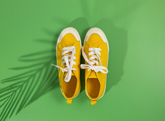 Yellow sneakers on green background with tropical leaf shadow. Trendy background. Mock up, summer holidays, vacation, travel, fashion concept