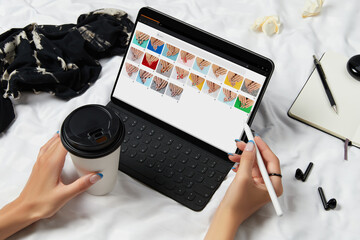 Womans hands and black tablet with manicure designs on screen over white bed. Beauty salon concept