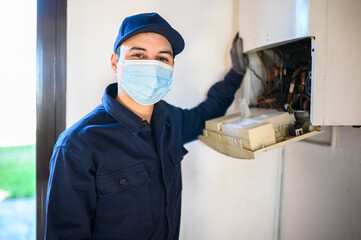 Obraz na płótnie Canvas Smiling technician repairing an hot-water heater wearing a mask, coronavirus concept