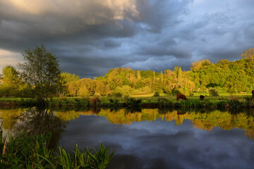 Stormy skies as the sun sets over the River Wey and meadows in Godalming, Surrey, UK