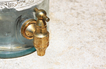 Fototapeta na wymiar Antique vessel close-up with copper faucet for pouring liquid on brown background