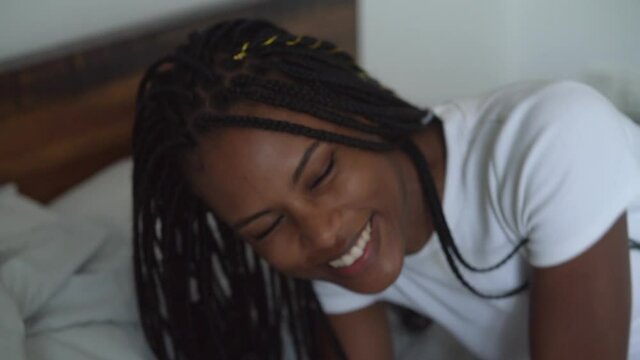 Young black woman with braided hair falling on bed and smiling