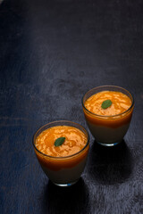 Two glasses of delicious mango lassi drink decorated with mint leaves in black wooden background.