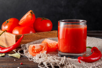 glass of tomato juice, slices of fresh red tomato, chili pepper, spices on a rustic napkin on a wooden