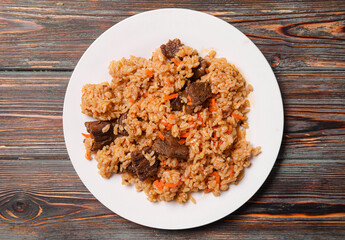 Uzbek pilaf with meat on a white plate on a dark wooden background top view