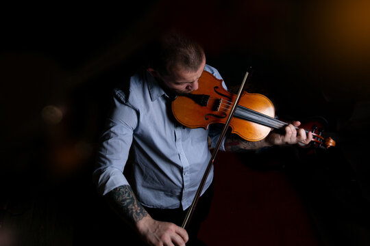 A man in a blue shirt plays the violin on a black background