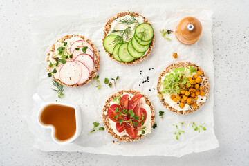 Four crispy buckwheat bread with cream cheese, radish, tomato, chickpea, cucumber and microgreen for healthy breakfast on parchment paper on grey stone background. Concept vegan and healthy eating.