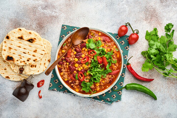 Mexican black bean soup with minced meat, tomato, cilantro, avocado and vegetables stew on a light grey slate, stone or concrete background. Traditional Mexican dish. Top view with copy space.