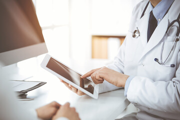 Unknown male doctor and patient woman discussing current health examination while sitting in sunny...