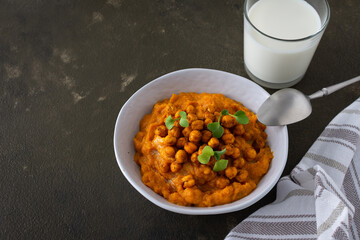 Thick pumpkin soup with baked chickpeas and radish sprouts in a plate with a glass of milk on the table, delicious healthy dinner