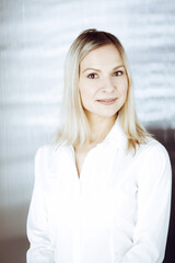 Friendly adult business woman standing straight. Business headshot or portrait in sunny office