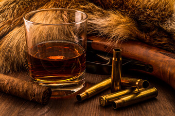 Hunting rifle with glass of whiskey and cuban cigar lying next to the animal's fur produced. View...