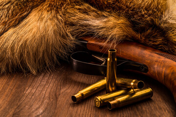 Hunting rifle lying next to the animal's fur produced with the casings from bullets. View close-up,...