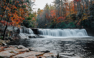 Hooker Falls, a waterfall of the Little River surrounded by colorful fall foliage on a gloomy, cloudy day in DuPont State Recreational Forest, Hendersonville, North Carolina, USA. Long exposure.