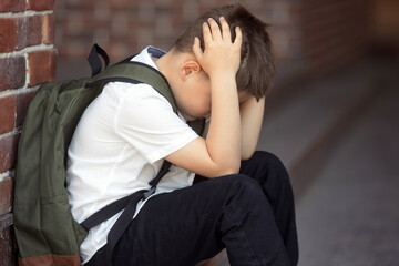 Upset boy sitting at school and crying after bullying by pupils classmates