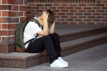 Upset boy sitting at school and crying after bullying by pupils classmates