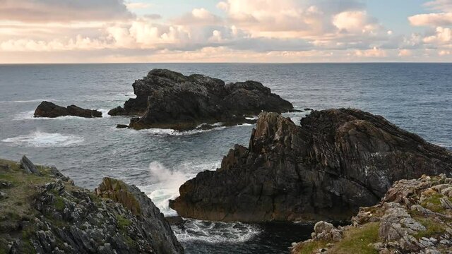 Waves crashing on rocks and seagulls in flight at Butt of Lewis, Isle of Lewis, Outer Hebrides, Scotland. Taken at sunset with pink clouds on the horizon. Slow motion.