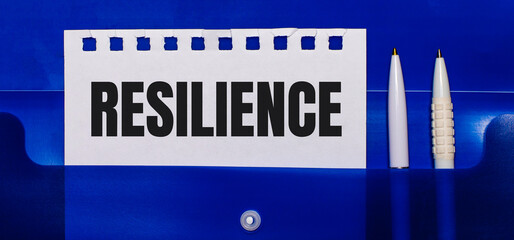 On a blue background, white pens and a sheet of paper with the text RESILIENCE