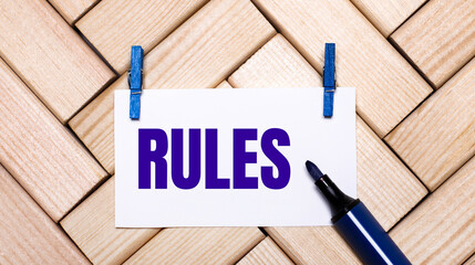 On a wooden background, a white card with the text RULES on blue clothespins and a blue marker. View from above