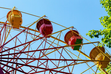 Bottom view of bright yellow and red Ferris wheel booths in an amusement park against a blue sky.