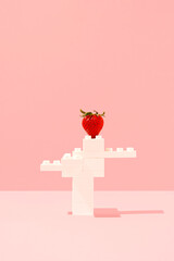 Red strawberry on white plastic toy bricks construction against pink background. Minimal summer...